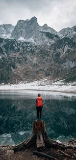 Hiker stands by a peaceful lake with towering mountains in the background.