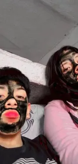 Two individuals with charcoal facial masks taking a selfie.