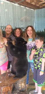 Family enjoys playful moment with bear cub in rustic outdoor setting.