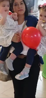 Mother holding twins with a red balloon in a mall setting.