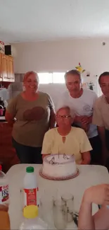 A family celebrating around a cake, smiling warmly in a cozy home setting.