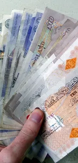 Hand holding fanned British banknotes on light grey background.