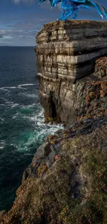 Majestic dragon on a cliff by the ocean under a vast sky.