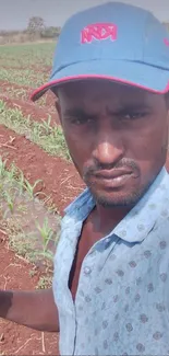 A man takes a selfie in a farm field with crops and earthy background.