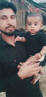 A father holding his baby in a rustic outdoor setting.