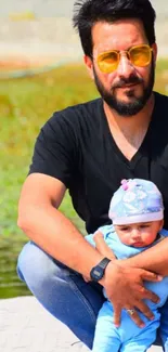 Father with baby outdoors on a sunny day, wearing casual clothing.