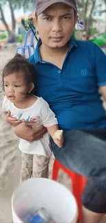 Father in blue shirt holding child at the beach.