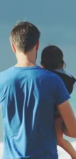 Father holding child at the beach, serene ocean scene.