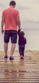 Father and child walking on beach boardwalk towards the ocean.