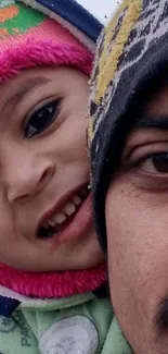 Father and child smiling outdoors in winter clothes on a rooftop.