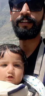 Father and child smiling outdoors with mountain backdrop.