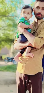 Father holding child outdoors with green background.