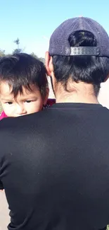 Father holding child outdoors on a sunny day.