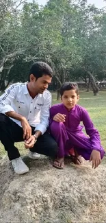 Father and child sitting outdoors on grass in the park.