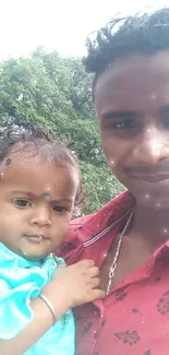 Father holding child outdoors with lush green background.