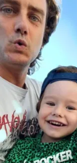 Father and child smiling with a blue sky background.