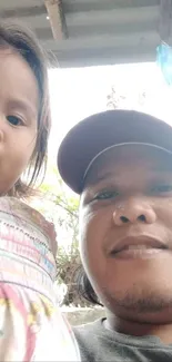 Father holding young daughter outdoors under a roof.