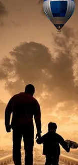 Father and son silhouetted against sunset with hot air balloon.