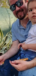 Father and son together outdoors with plants and sunny backdrop.