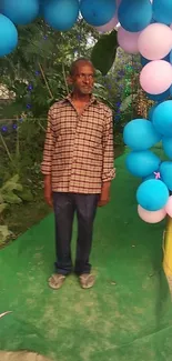 Man standing under colorful balloon arch outdoors.