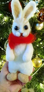 Felt bunny with red scarf in front of Christmas tree.