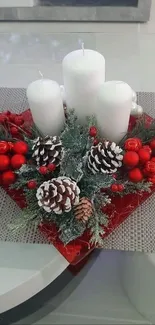 Elegant centerpiece with candles, red berries, and pine cones on a table.