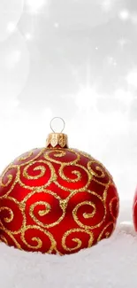 Red Christmas ornament with golden swirls in snow.