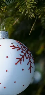 Christmas ornament with red snowflake pattern on green pine tree.