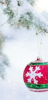 Bright red Christmas ornament on snow-covered pine branch.