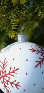 White Christmas ornament with red snowflakes hanging on green pine.