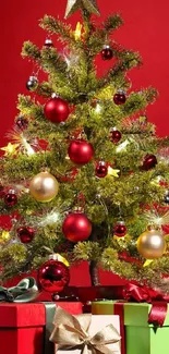 Festive Christmas tree with red ornaments and gift boxes against a red background.