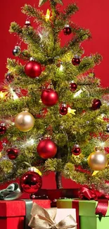 Festive Christmas tree with red ornaments and gift boxes against a red background.