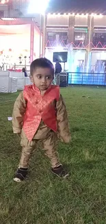 Child in traditional attire at a festive event, standing on grass.