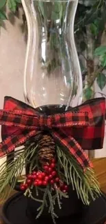 Festive glass candle holders with plaid ribbons and winter decorations on a wooden table.