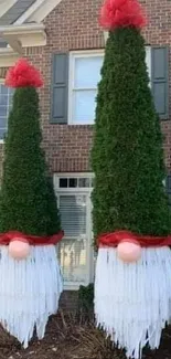 Gnome-shaped trees decorated as Christmas gnomes in a brick house front yard.