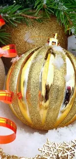 Golden Christmas ornament with ribbon on snow and fir branches.