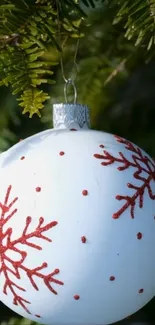 White ornament with red snowflakes on pine tree.