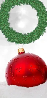 Red Christmas ornament with green wreath on snowy background.