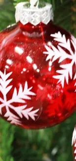 Red Christmas ornament with snowflakes hanging on a tree.