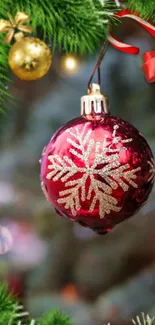 Red Christmas ornament with gold snowflake hang on a tree surrounded by greenery.