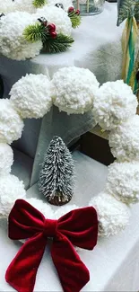 Festive holiday wreath with red bow and pom-poms displayed on a table.