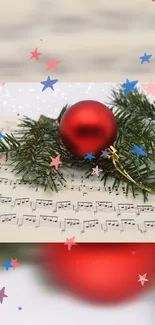 Red ornament on pine branch with sheet music and colorful stars.