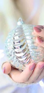 Hands holding a glittering ornament with bokeh lights in the background.