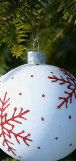 White ornament with red snowflakes hanging on a green pine tree.