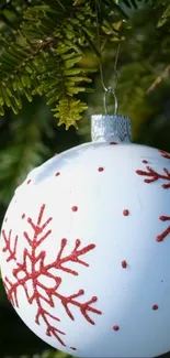 White Christmas ornament with red snowflakes on green tree.