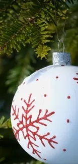 White ornament with red snowflake on a green pine branch.