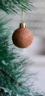 Glittery gold Christmas ornament hanging on a green pine branch.