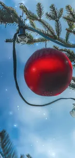 Red ornament hanging on a pine branch with a blue sky background.