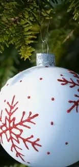 White ornament with red snowflakes on a green pine tree branch.