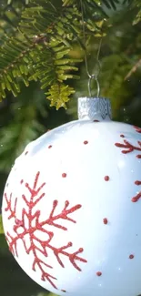 White Christmas ornament with red snowflakes hanging on a tree.